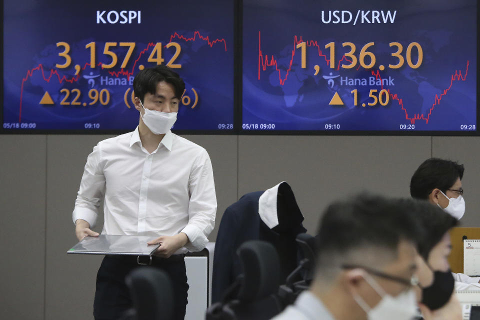 A currency trader walks near screens showing the Korea Composite Stock Price Index (KOSPI), left, and the foreign exchange rate between U.S. dollar and South Korean won at the foreign exchange dealing room of the KEB Hana Bank headquarters in Seoul, South Korea, Tuesday, May 18, 2021. Asian shares rose Tuesday, partly on bargain-hunting from the recent global market falls amid continuing pessimism about the coronavirus pandemic. (AP Photo/Ahn Young-joon)