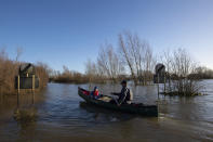 Anthony Gleave and his son Arthur, 3, canoe along the flooded A1101 in Welney, Norfolk, England, Sunday, Dec. 27, 2020. Hurricane-force winds reaching up to 106 miles per hour (170 kph) and rainstorms battered parts of Britain, disrupting train services and stranding drivers in floodwaters. The Isle of Wight saw Storm Bella’s strongest winds at 106mph, while parts of the south coast of England and north Wales also saw gusts of around 80mph (129 kph). (Joe Giddens/PA via AP)