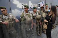 Lebanese stand guard in front of a depositor who is protesting and nock by a placard on a fortified bank gate, in Beirut, Lebanon, Friday, Sept. 24, 2021. Dozens of Lebanese depositors protested throwing eggs and tomatoes on a number of private banks in central Beirut, demanding to have access to their deposits which have been blocked under informal capital controls since the country's financial and economic crisis began in late 2019. (AP Photo/Hussein Malla)