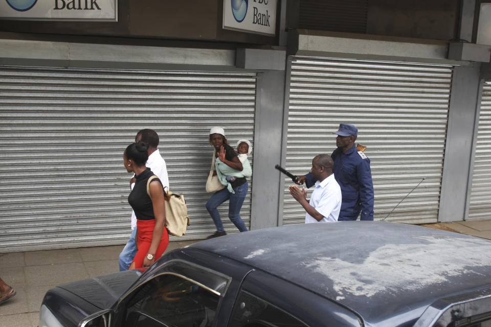 A woman carrying a baby runs from police while walking near the opposition party headquarters in Harare, Wednesday, Nov. 20, 2019. Zimbabwean police with riot gear fired tear gas and struck people who had gathered at the opposition party headquarters to hear a speech by the main opposition leader Nelson Chamisa who still disputes his narrow loss to Zimbabwean President Emmerson Mnangagwa. (AP Photo/Tsvangirayi Mukwazhi)