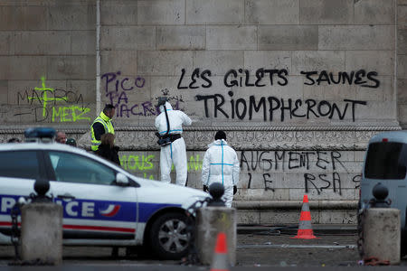 Police work around the message, "The Yellow Vests will Triumph" written on the Arc de Triomphe, the morning after clashes with protesters wearing yellow vests, a symbol of a French drivers' protest against higher diesel taxes, in Paris, France, December 2, 2018. REUTERS/Benoit Tessier