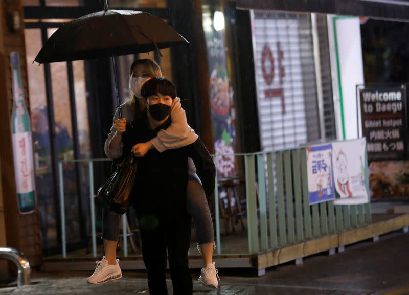 A man wearing a protective mask carries a woman on his back in a bar district amid the rise in confirmed cases of the coronavirus disease (COVID-19) in Daegu
