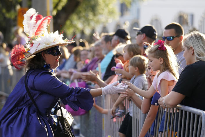 A woman dressed in period costume hands a trinket to a child during a parade dubbed "Tardy Gras," to compensate for a cancelled Mardi Gras due to the COVID-19 pandemic, in Mobile, Ala., Friday, May 21, 2021. (AP Photo/Gerald Herbert)