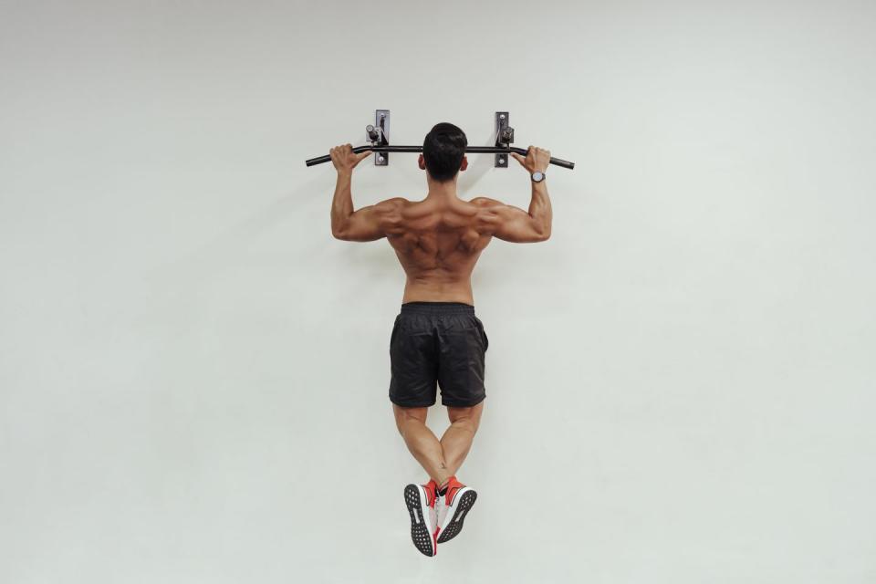 mid adult sportsman doing chin ups with exercise equipment on white wall