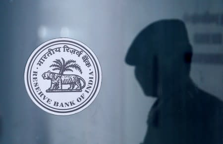 A security guard's reflection is seen next to the logo of the Reserve Bank Of India (RBI) at the RBI headquarters in Mumbai