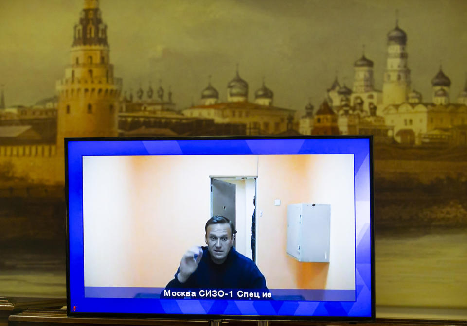 Russian opposition leader Alexei Navalny appears on a TV screen during a live session with the court during a hearing of his appeal in a court in Moscow, Russia, Thursday, Jan. 28, 2021, with the wall with the image of the Moscow Kremlin in the background. Navalny was jailed soon after arriving to Moscow after authorities accused him of violating of the terms of his 2014 fraud conviction. A court on Thursday is to hear an appeal on the ruling to remand him into custody. Next week, another court will decide whether to send him to prison for several years for the alleged violations. (AP Photo/Alexander Zemlianichenko)