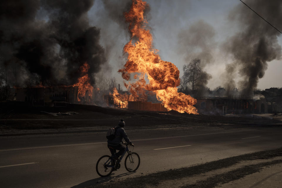 FILE - A man rides his bike past flames and smoke rising from a fire following a Russian attack in Kharkiv, Ukraine, on March 25, 2022. With its aspirations for a quick victory dashed by a stiff Ukrainian resistance, Russia has increasingly focused on grinding down Ukraine’s military in the east in the hope of forcing Kyiv into surrendering part of the country’s eastern territory to end the war. If Russia succeeds in encircling and destroying the Ukrainian forces in Donbas, the country’s industrial heartland, it could try to dictate its terms to Kyiv -- and possibly attempt to split the country in two. (AP Photo/Felipe Dana)
