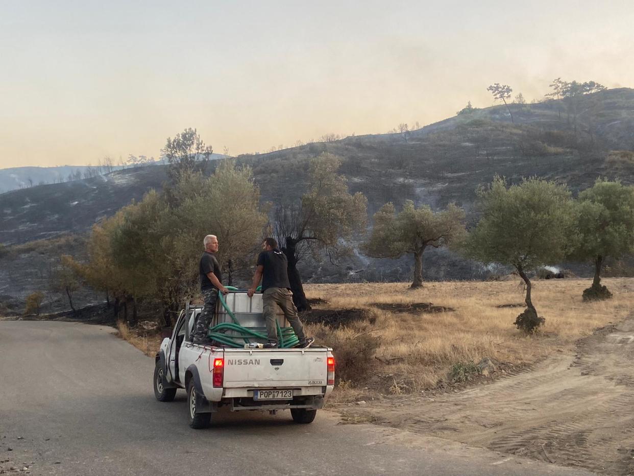 Volunteer firefighters survey the charred remains of trees which could smoulder for days near Vati (Andy Gregory/The Independent)