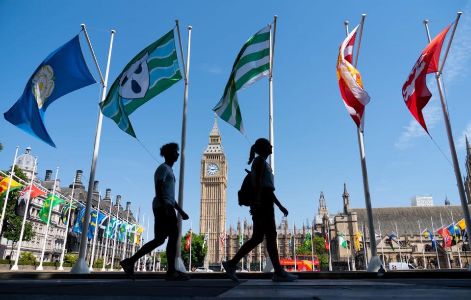 People walk in the shade past national flags in Parliament Square, central London (Dominic Lipinski/PA) (PA Wire)