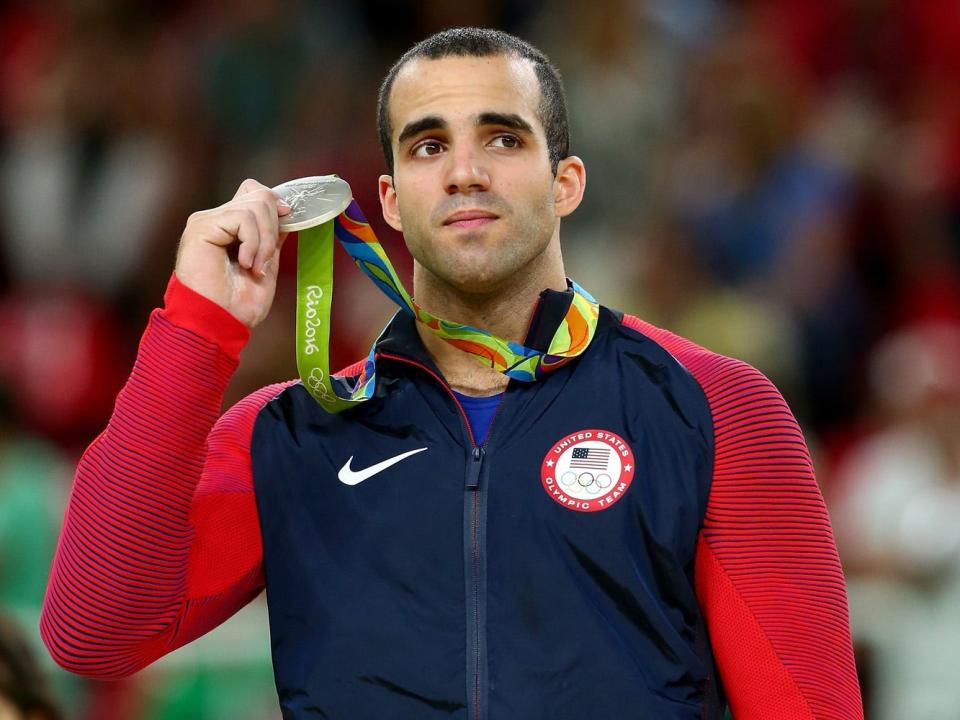 danell leyva holding up his medal in front of blurred out crowd