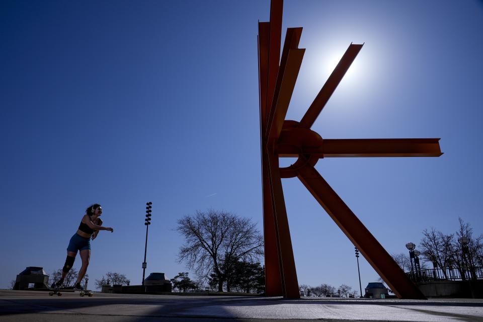 A woman skateboards near a sculpture as she enjoys unseasonably warm weather Tuesday, Feb. 27, 2024, in Milwaukee. (AP Photo/Morry Gash)