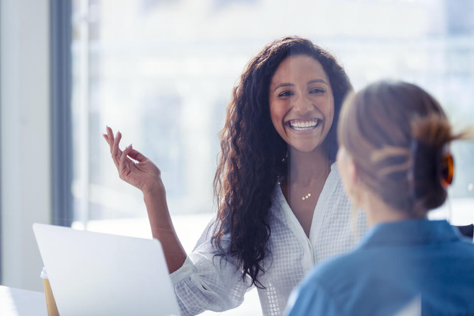 stay interview Business colleagues having a conversation. They are both young business people casually dressed in a modern office. Could be an interview or consultant working with a client. She is listening and smiling. One person has her back to us. Mixed ethnic group. One is African American and the other is Caucasian