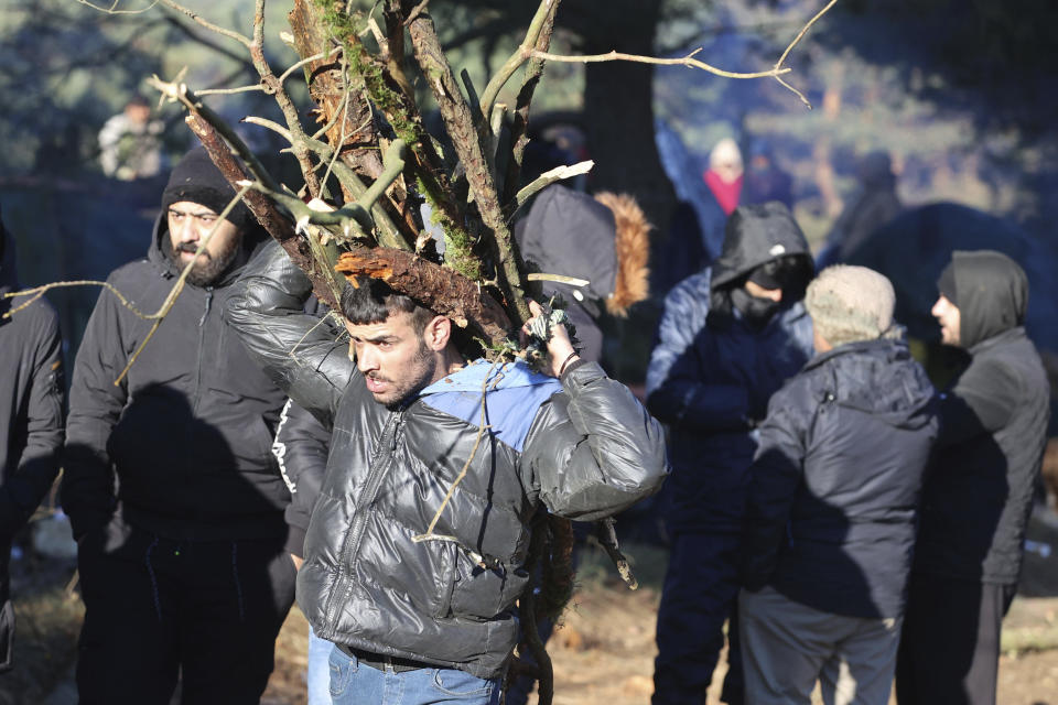 A migrant carries firewood as other migrants from the Middle East and elsewhere gather at the Belarus-Poland border near Grodno, Belarus, Tuesday, Nov. 9, 2021. Polish riot police and coils of razor wire faced off Tuesday against migrants, including families with young children, who were camped just across the border in Belarus, amid a tense standoff on the European Union's eastern border. (Leonid Shcheglov/BelTA via AP)