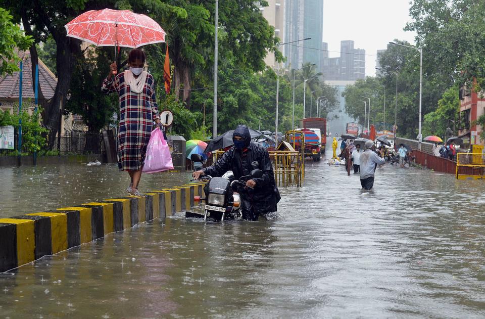 A motorist pushes his stalled bike while a woman walks on a road divider during a heavy monsoon rainfall in Mumbai on August 4, 2020. Photo by SUJIT JAISWAL/AFP via Getty Images)