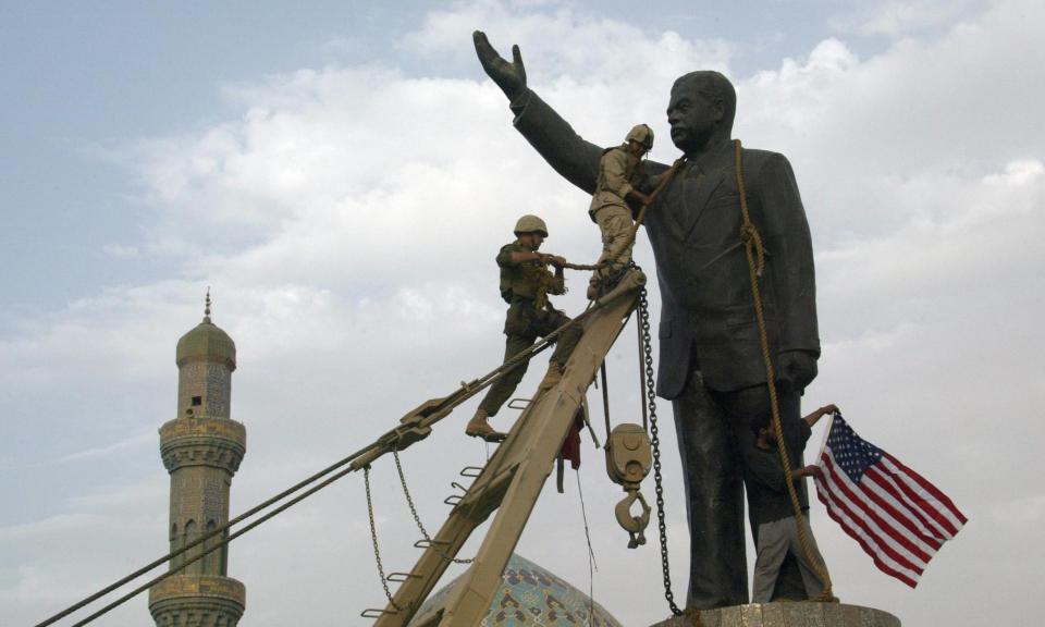 U.S. Marines chain the head of a statue of Saddam Hussein before pulling  it down in Baghdad's al-Fardous square April 9, 2003, while an Iraqi  waves the U.S. flag. / Credit: RAMZI HAIDAR/AFP/Getty Images