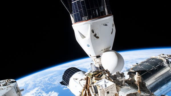 two cone-shaped spacecraft docked at the International Space Station, Earth in the background