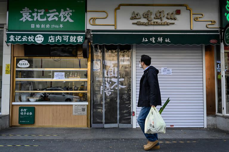 Un hombre con una bolsa de verduras pasa por delante de las tiendas cerradas en el distrito de Chaoyang de Pekín debido a las restricciones por el coronavirus Covid-19 el 19 de noviembre de 2022.