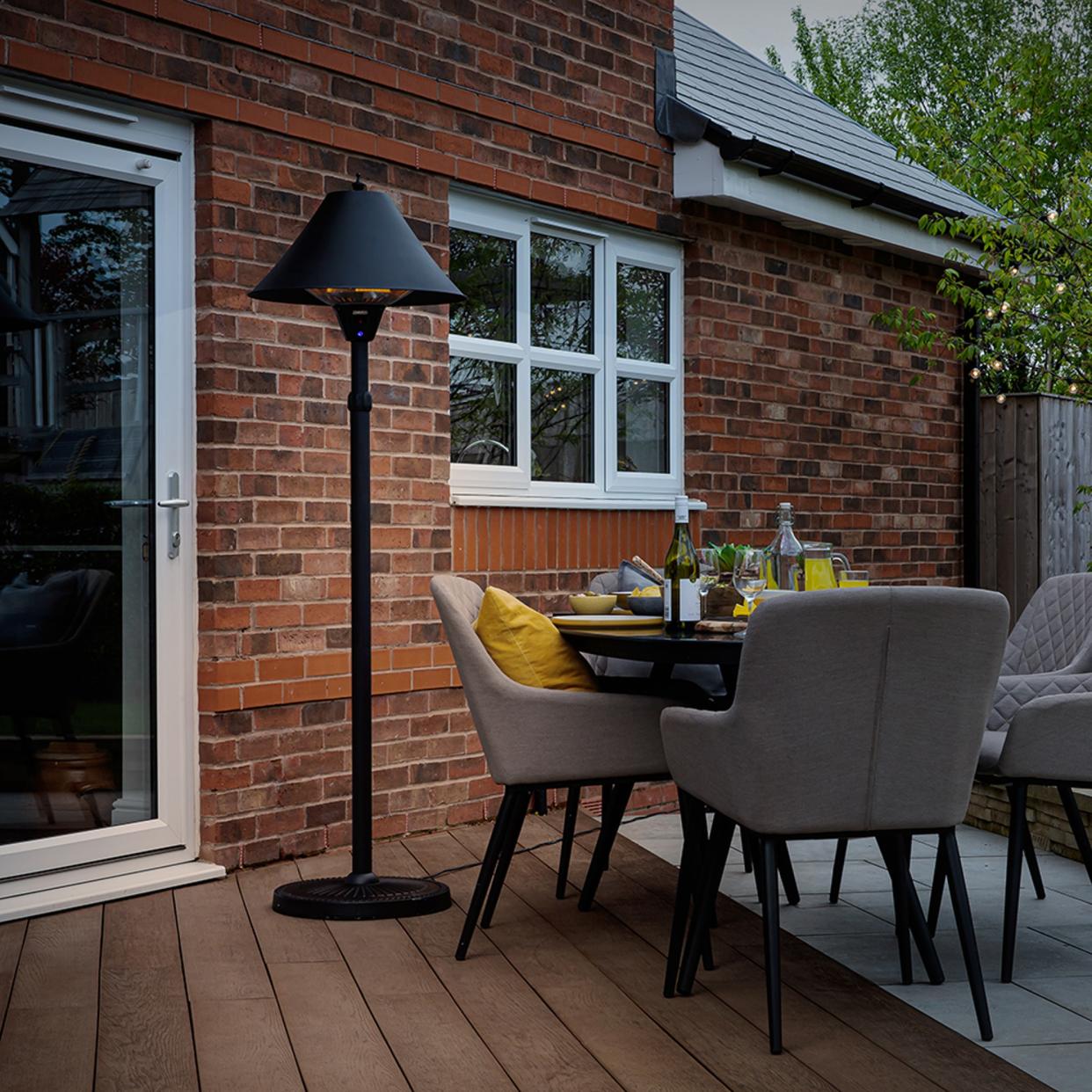  Zanussi 2100W Black Adjustable Freestanding Patio Heater in a garden with tables and chairs. 