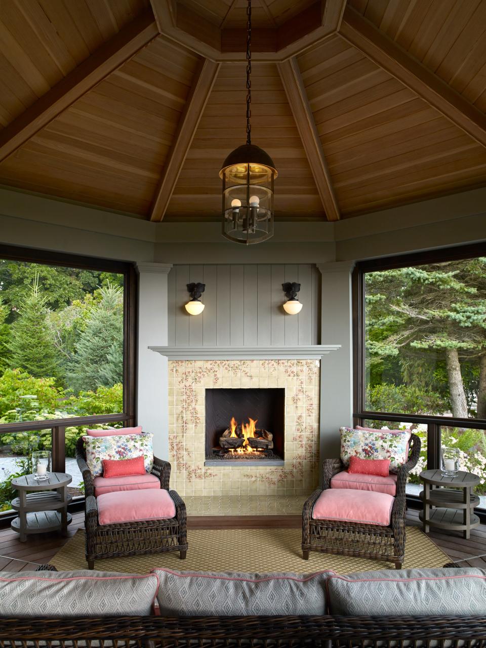 The three-season porch is a favorite perch. The custom tiles on the fireplace were hand-painted by D. Todd & Co. and installed by Old Port Specialty Tile. The pendant lighting is by Rocky Mountain Hardware. The sconces are by Rejuvenation. Lippmann found the weathered teak side tables, lounge chairs, and ottomans at Janus et Cie.