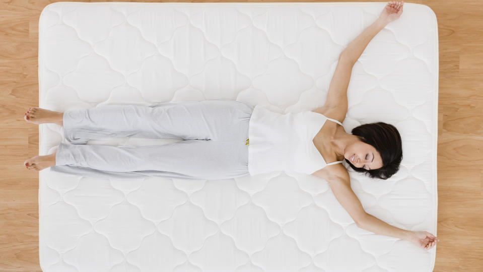 A woman sleeps happily on a white mattress placed on the floor