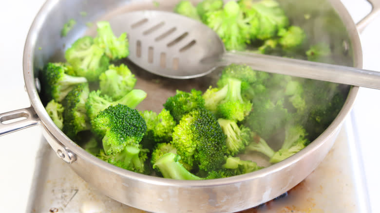 Steamed broccoli in a pan with slotted spoon