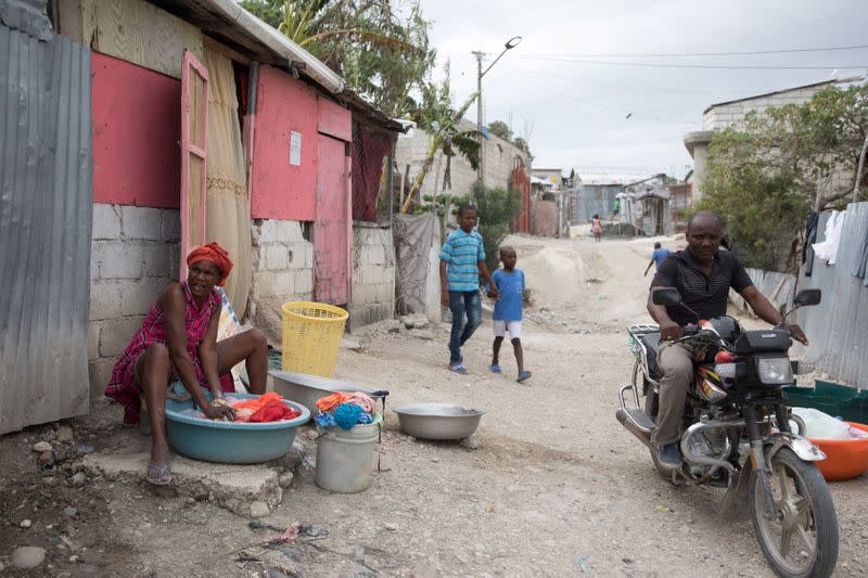 Man drives a bike past a woman doing laundry in a street of Caradeux, a camp for people displaced by the January 2010 earthquake, in Port-au-Prince