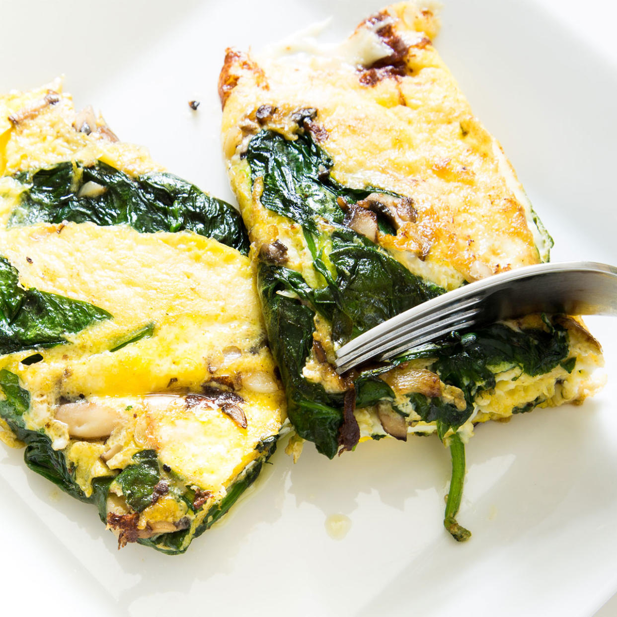 fork cutting into a spinach and mushroom omelette