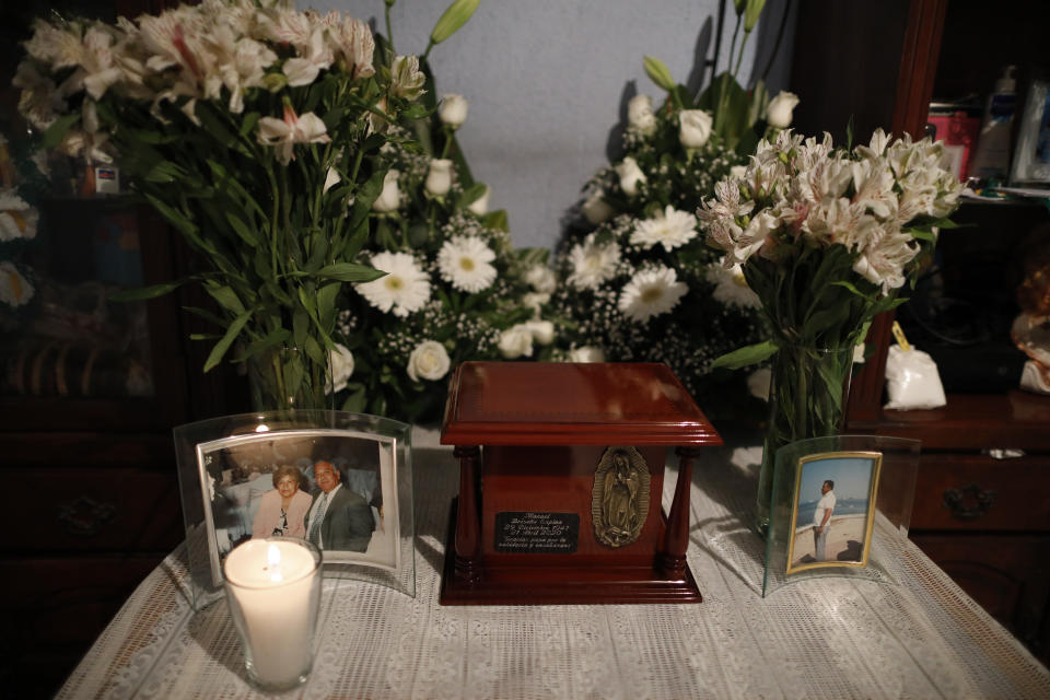 Flowers and pictures surround the urn containing the ashes of Manuel Briseno Espino, 78, who died from complications due to COVID-19, at the home where he lived with his family in the Iztapalapa district of Mexico City, Wednesday, April 22, 2020. Due to social distancing restrictions, the seven family members from three generations who lived with Briseno marked his passing with quiet prayers at home, unable to invite his many friends or other relatives, or to bury him in the cemetery plot with his late wife of 49 years, Consuelo Garcia Rodriguez. (AP Photo/Rebecca Blackwell)