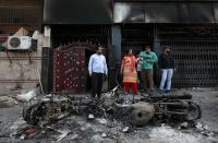 People stand next to the wreckages of motorcycles that were set on fire by a mob in a riot affected area after clashes erupted between people demonstrating for and against a new citizenship law in New Delhi