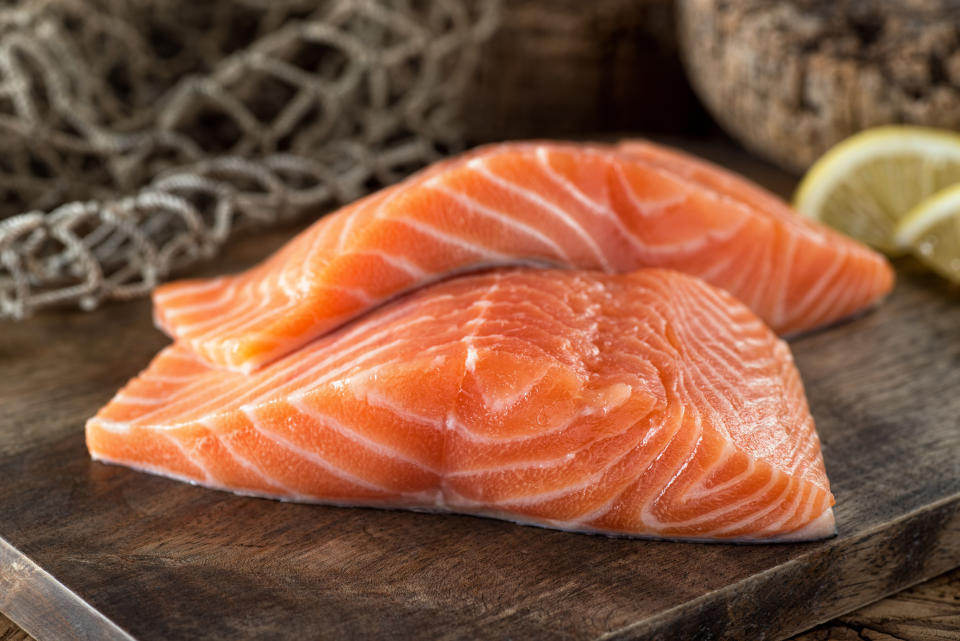 Fresh raw salmon fillets on a wooden board with lemon and fish net background