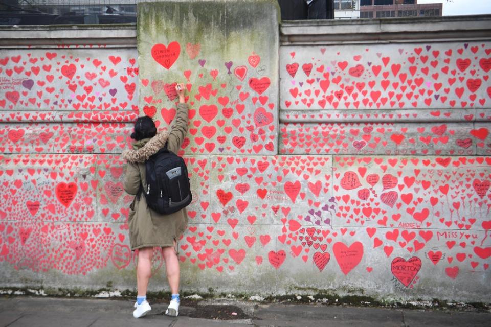 A woman writes in a heart on the Covid memorial wall on the Embankment in London (Victoria Jones/PA) (PA Wire)