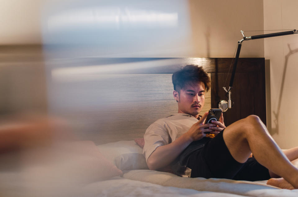 A young asian young man travelling to Barcelona, Spain, relaxing in his hotel room, using phones, taking notes and working with his smart devices.