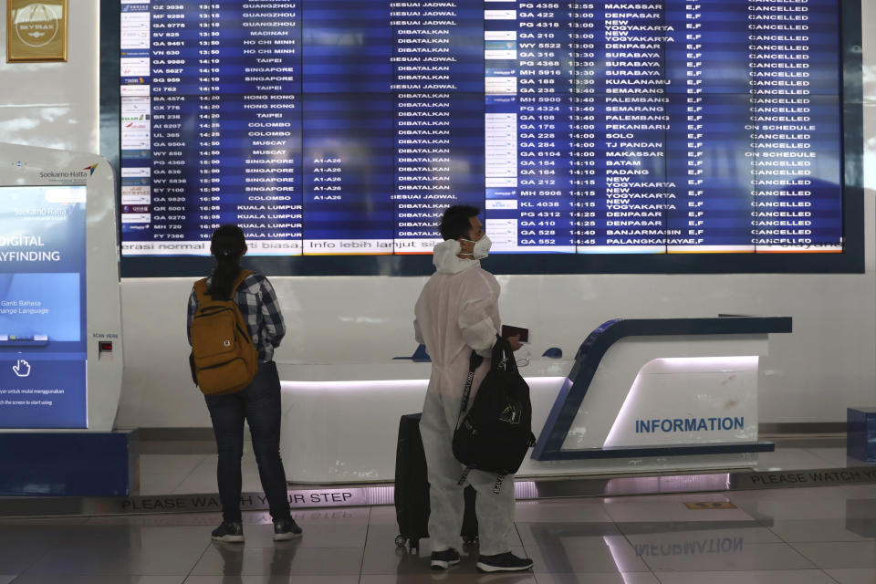 People watch an information screen with most of flights being cancelled at Soekarno-Hatta International Airport in Tangerang, Indonesia, Indonesia on Friday, April 24, 2020. Indonesia is suspending passenger flights and rail service as it restricts people in the world's most populous Muslim nation from traveling to their hometowns during the Islamic holy month of Ramadan because of the coronavirus outbreak.(AP Photo/Tatan Syuflana)