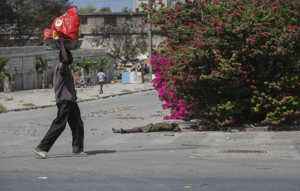 A lifeless body lies in the street as pedestrians walk past in Port-au-Prince, Haiti, Monday, March 25, 2024. According to witnesses, the man died during an attack by armed gangs. (AP Photo/Odelyn Joseph)