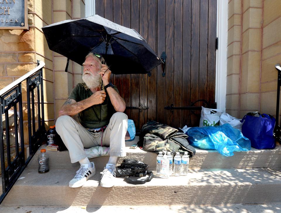 Brian Kearns, who is homeless, uses a umbrella to keep the sun off him as the temperature rises during the day as he sits on the steps of the Grace Lutheran Church on 7th Street Thursday, August 24, 2023.