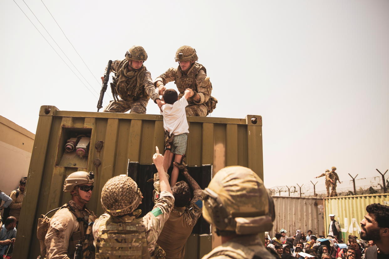 UK coalition forces, Turkish coalition forces, and U.S. Marines assist a child during an evacuation at Hamid Karzai International Airport, Kabul, Afghanistan, in this photo taken on August 20, 2021.  (Sgt. Victor Mancilla/U.S. Marine Corps/Handout via Reuters)