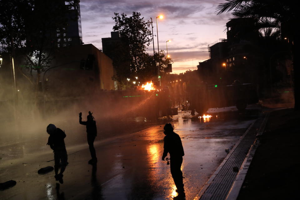 Anti-government protesters face off with a police water cannon in Santiago, Chile, Friday, Nov. 1, 2019. Chile has been facing days of unrest, triggered by a relatively minor increase in subway fares. The protests have shaken a nation noted for economic stability over the past decades, which has seen steadily declining poverty despite persistent high rates of inequality. (AP Photo/Rodrigo Abd)