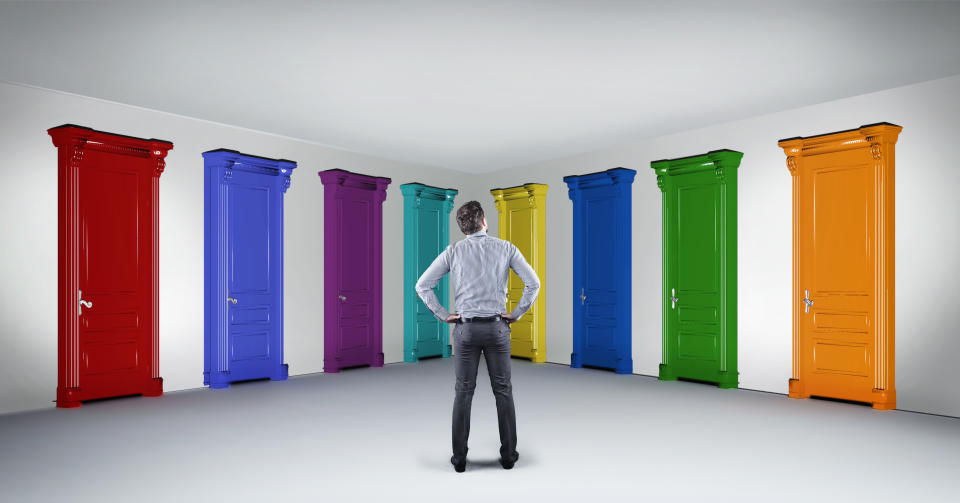 Businessman standing in hallway in front of multicolored doors. Concept of hard choice and opportunities.