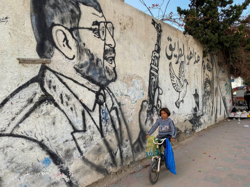 A Palestinian boy rides a bicycle past a mural depicting late Hamas leader Abdel-Aziz Al-Rantissi in Gaza City