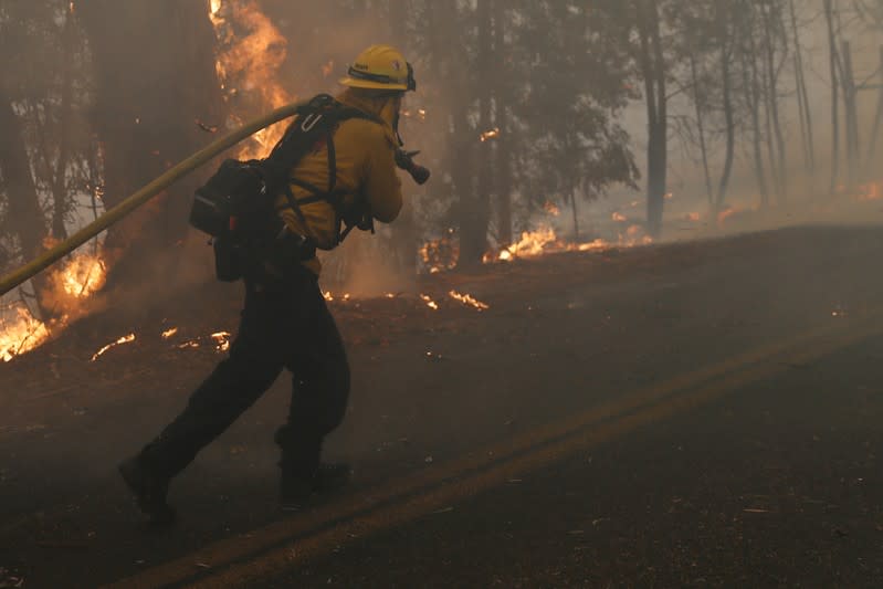 A firefighter pulls a hose along Chalk Hill Road as he battles the wind-driven Kincade Fire in Windsor, California