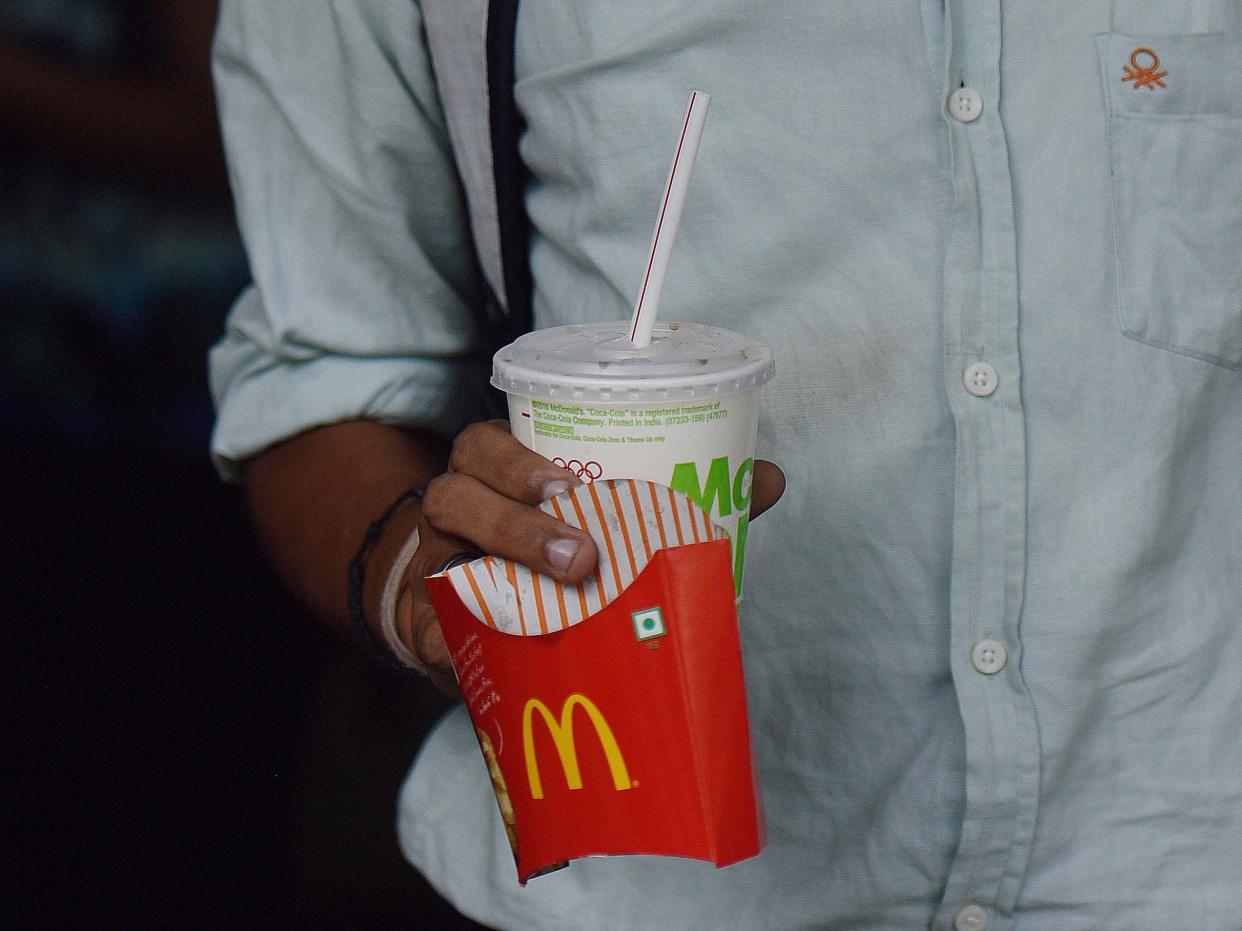 A man holding an empty box of McDonald's fries and a soda cup in his right hand in a dimly lit room.