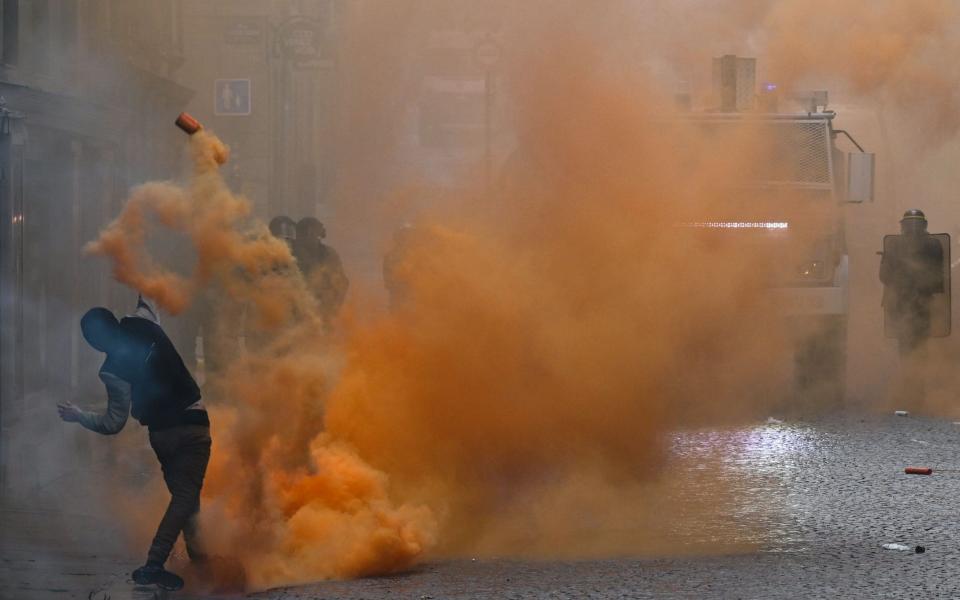 A protestor throws a cannister of orange smoke towards French riot police - DAMIEN MEYER/AFP via Getty Images