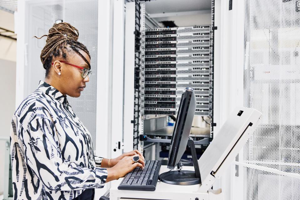Black female IT professional configures server in data center.