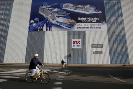 FILE PHOTO Shipbuilders ride past a giant poster November 9, 2016 at the STX Les Chantiers de l'Atlantique shipyard site in Saint-Nazaire, western France. A South Korean court approved Italy's Fincantieri SpA as preferred bidder to buy shipbuilder STX France, the court spokesman said January 3, 2017. REUTERS/Stephane Mahe/File Photo