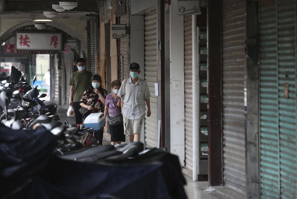 People wear face masks to help protect against the spread of the coronavirus walk past a row of closed shops after the COVID-19 alert rose to level 3 in Taipei, Taiwan, Tuesday, May 18, 2021. (AP Photo/Chiang Ying-ying)