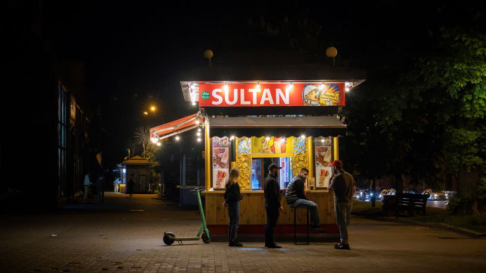 People stand at a fast-food stall in Kyiv during a partial blackout. - Thomas Peter/Reuters