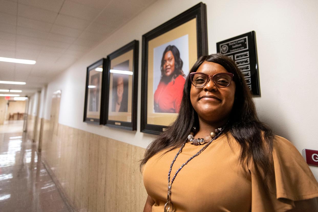 Peoria County Auditor Jessica Thomas stands by a row of portraits of county auditors outside of her office in the Peoria County Courthouse. Proposed budget cuts by the Peoria County Board could remove her three staff members.