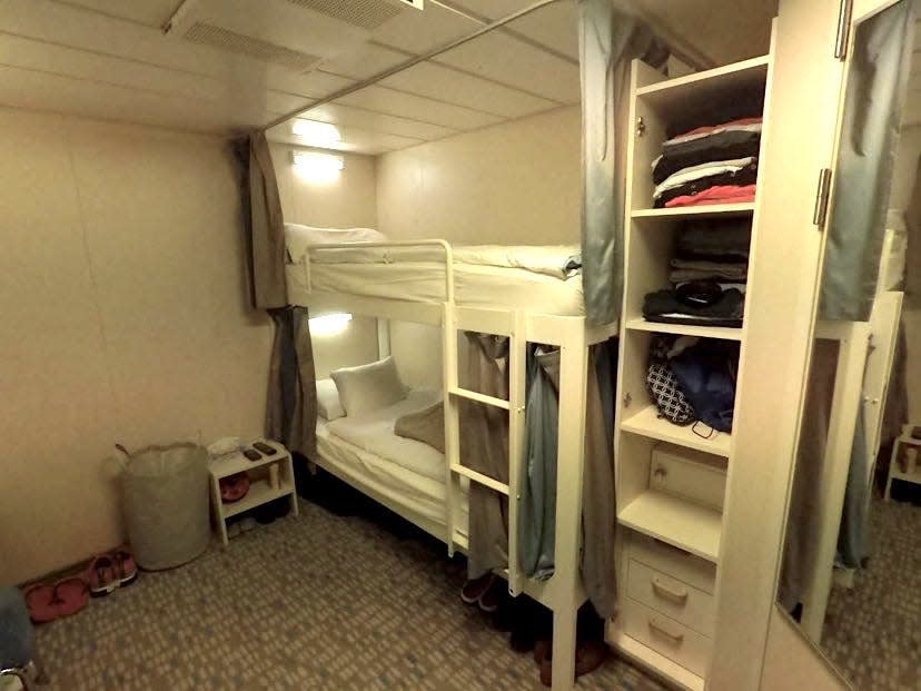 A crew cabin onboard the cruise ship with bunk beds, a small closet and white walls