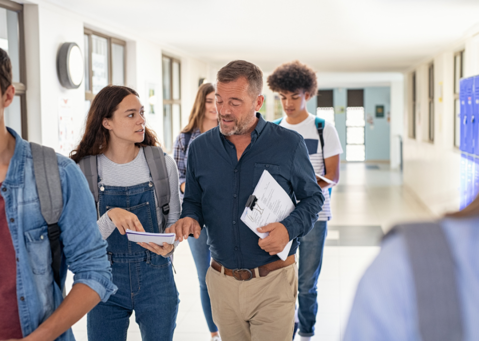 A student talking to a teacher in the hallway.