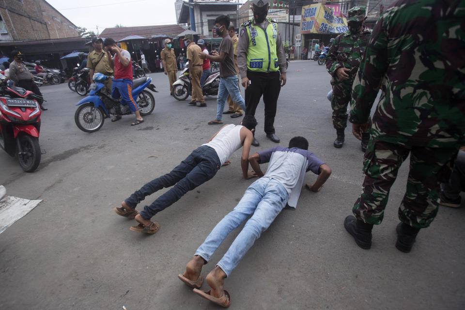 An Indonesian policeman and soldiers watch men do push-ups as a punishment for violating city regulation requiring people to wear face masks in public places as a precaution against coronavirus outbreak, in Medan, North Sumatra, Indonesia, Wednesday, Sept. 23, 2020. (AP Photo/Binsar Bakkara)